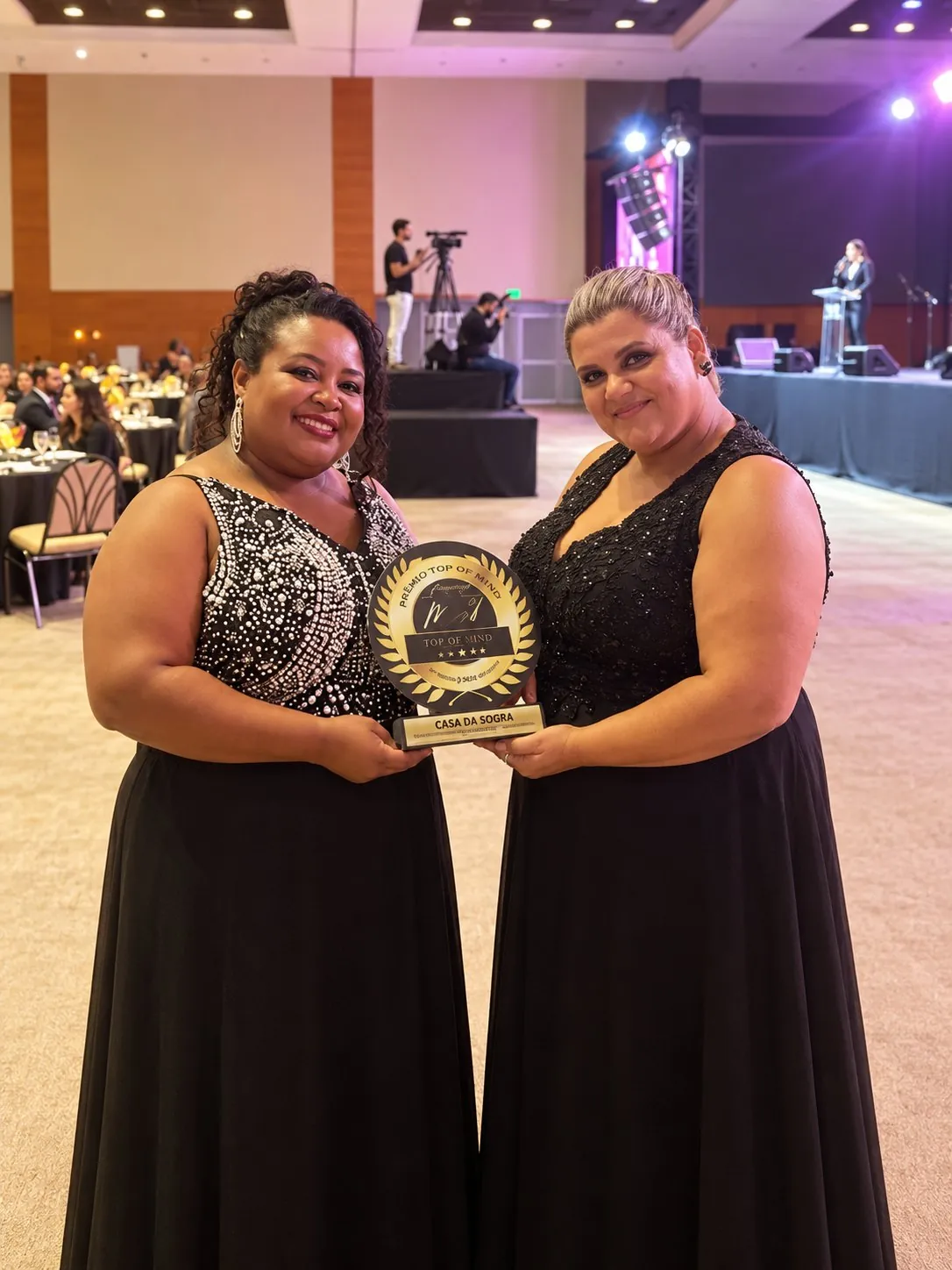 Duas representantes da Casa da Sogra segurando um troféu em evento